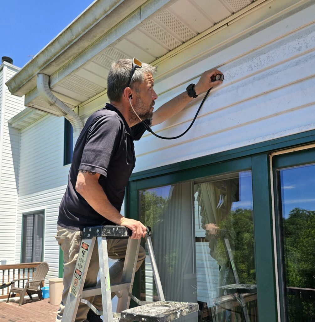 Pest control technician inspecting the exterior siding of a home in Fenton, MO 63026 for potential pest infestations.