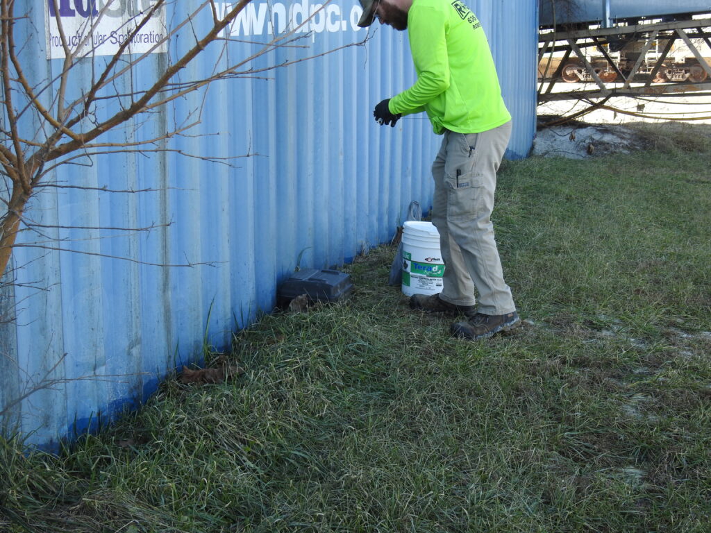 Technician refilling rodent bait station near commercial building in St. Louis.