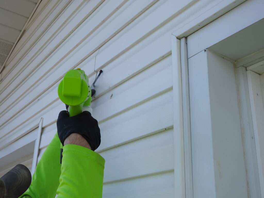Pest control technician injecting insect prevention treatment into siding crevice in O'Fallon, MO 63366.