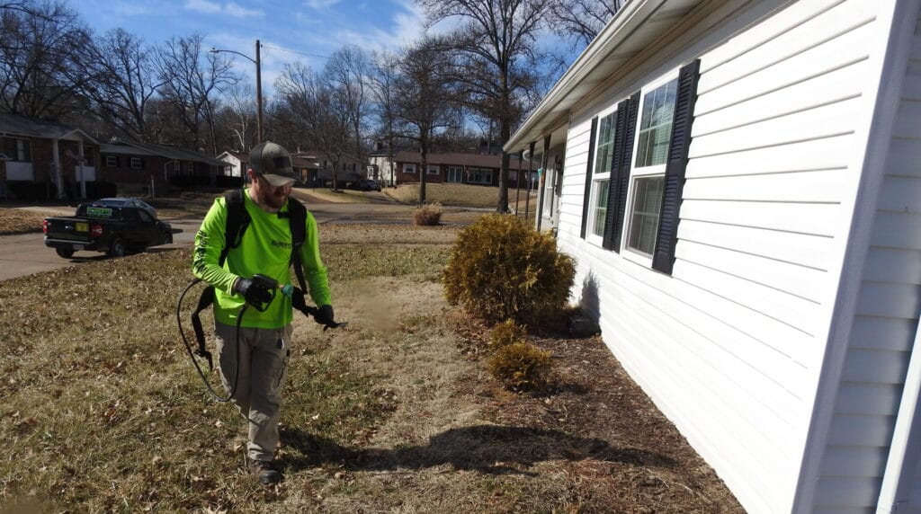 Pest control technician applying exterior treatment along the foundation of a residential home in Bonne Terre, MO 63628.