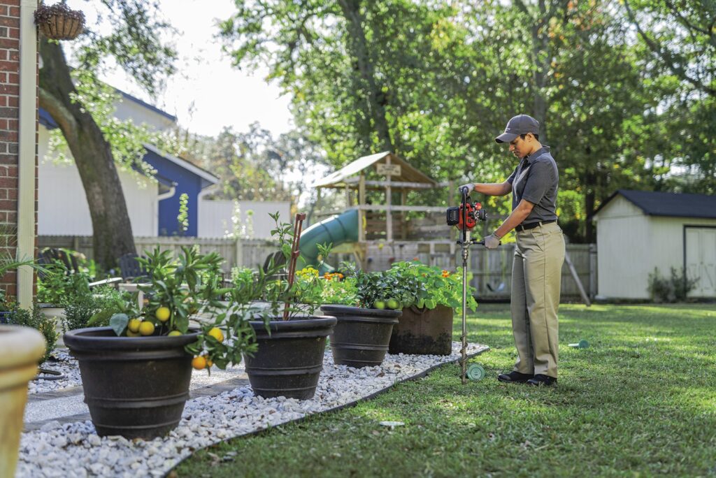 A pest control technician carefully treating a backyard garden and landscaping