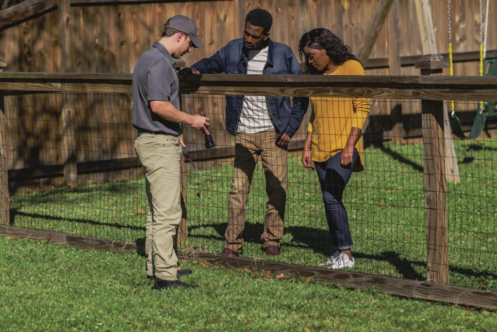 Pest control technician reviewing termite inspection findings with two homeowners in a backyard